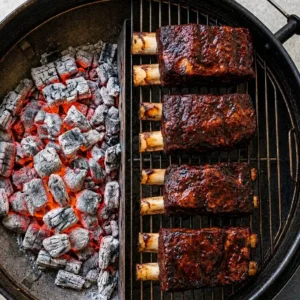 A top view of four beef ribeye steaks with a dark, glossy crust, cooked indirectly on a charcoal grill