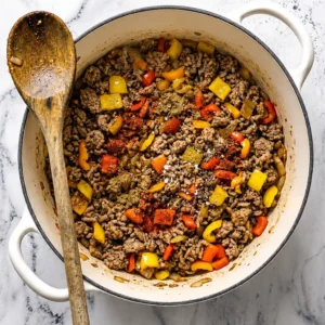 cooked ground turkey mixed with colorful diced bell peppers, aromatic spices, and seasonings inside a large white Dutch oven, with a wooden spoon resting on the rim.