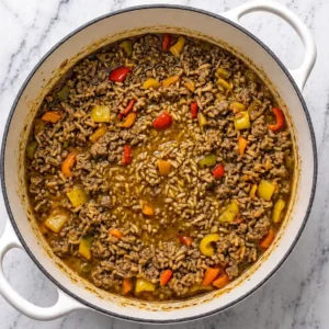 Cooked white rice, ground turkey, and diced bell peppers, simmered in a flavorful chicken broth in a white Dutch oven.
