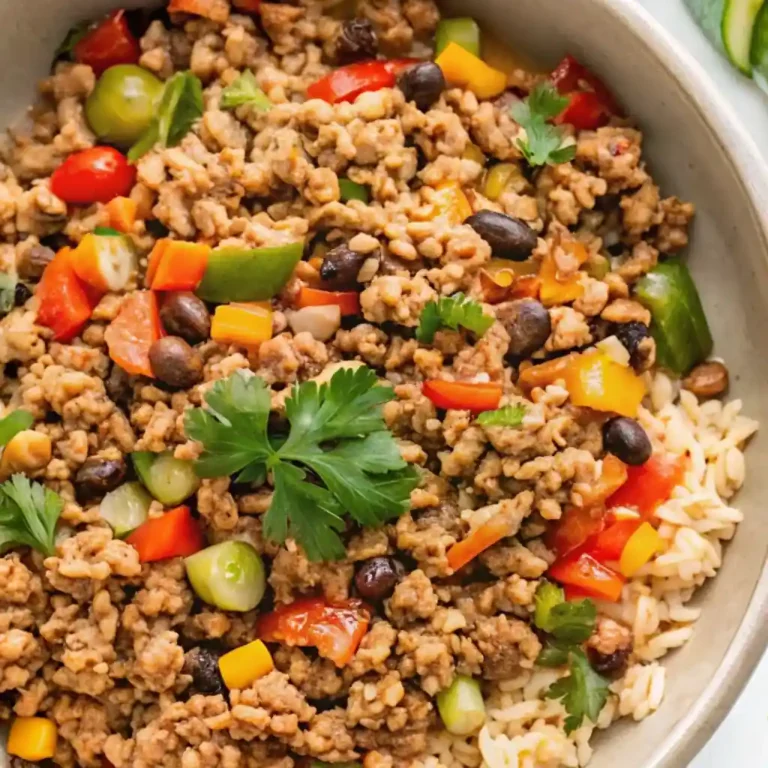 A white dish filled with minced turkey and cooked rice with colorful vegetables such as bell peppers and peas, garnished with fresh herbs, served as a healthy meal.