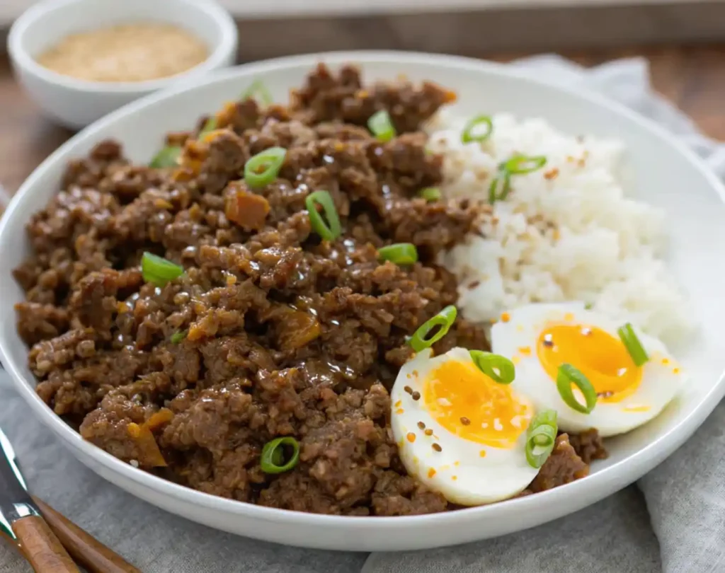 Ground Beef Bulgogi served with steamed white rice, an egg cut in half and covered with sesame seeds and green onions on a white plate.