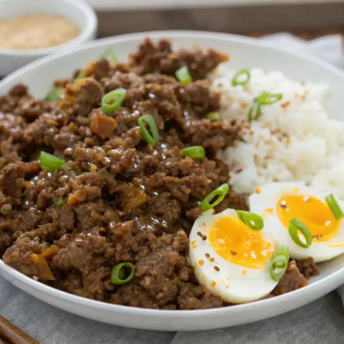 Ground Beef Bulgogi served with steamed white rice, an egg cut in half and covered with sesame seeds and green onions on a white plate.