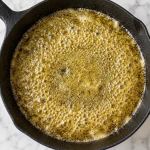 Oil is sizzling in a heavy black cast-iron skillet, which stands out against the backdrop of a light-colored marble countertop.