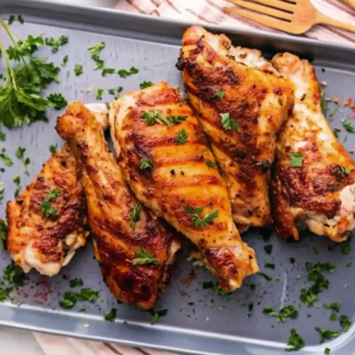 This image showcases a delicious serving of golden-brown baked turkey wings, perfectly seasoned and garnished with fresh parsley. The wings have a crispy, caramelized skin with visible grill