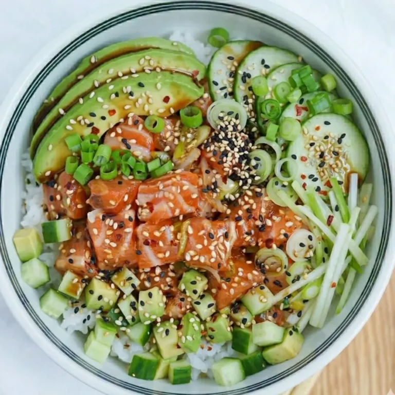 A vibrant salmon poke recipe featuring marinated raw fish, sliced avocado, cucumber rounds, and diced vegetables over white rice. Garnished with sesame seeds, chili flakes, and green onions in a bowl.