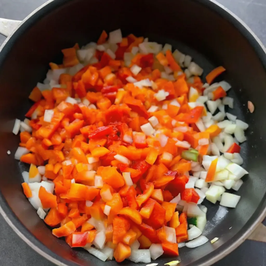 Diced white onions and red bell peppers are sautéed in a black pan as the aromatic base for a dish, likely the start of the Chicken Taco Soup.