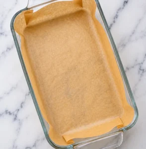 An empty glass rectangular baking dish lined with brown parchment paper, prepared for baking an Italian meatloaf recipe