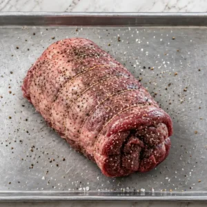 Raw tied venison roast seasoned generously with coarse salt and freshly cracked black pepper resting on a metal baking sheet.