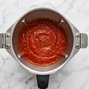A top-down view of smooth, bright red vindaloo spice paste freshly blended inside a metal blender container on a marble countertop.