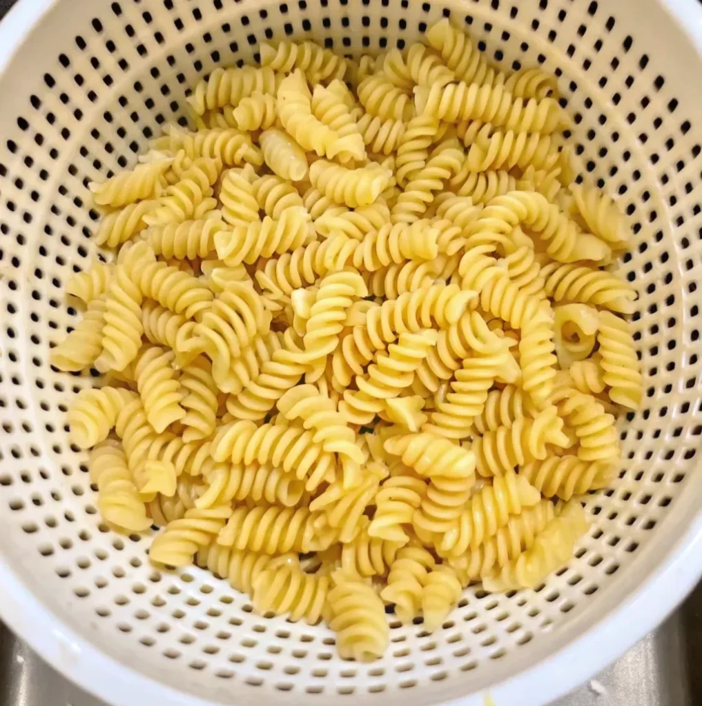 Cooked rotilli pasta draining in a white plastic colander. 