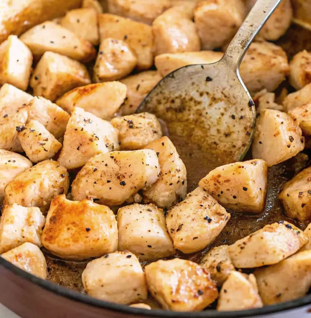 Diced cooked chicken breasts are sautéed in a stainless steel skillet with melted fat and spices,