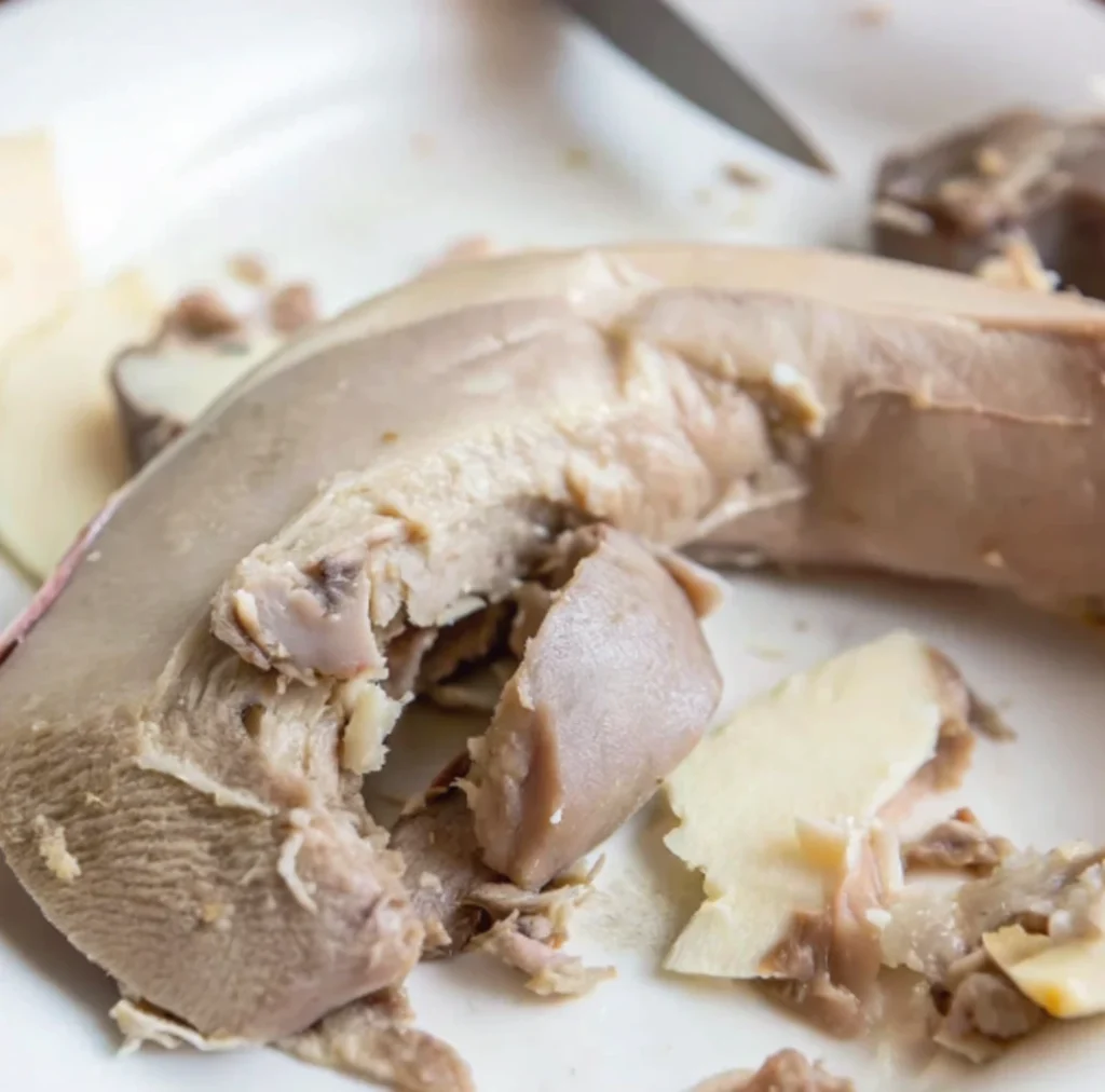 Cooked beef tongue, partially peeled and cut, resting on a white plate, revealing the tender meat texture,