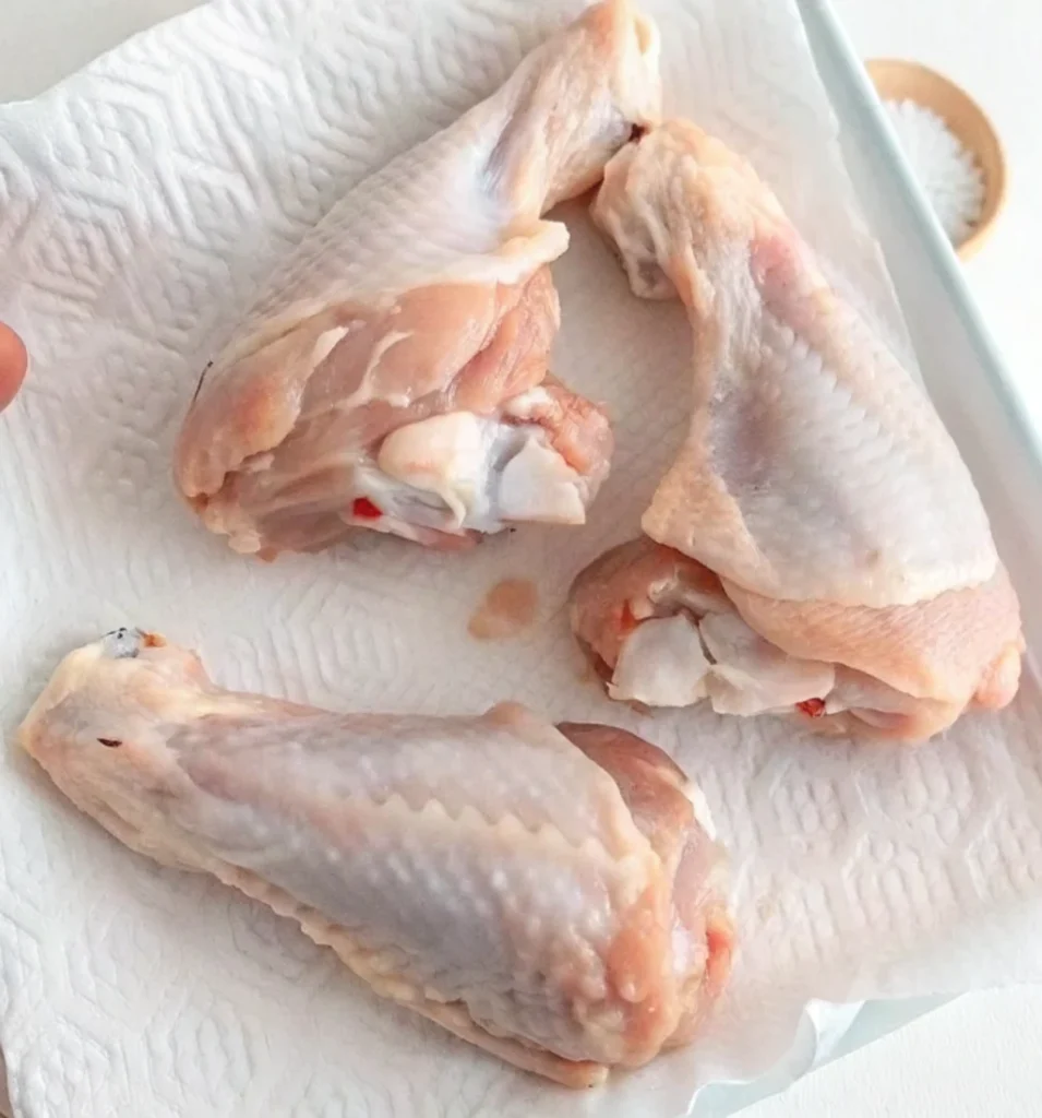 Three raw turkey wing drumettes are placed on a white paper towel, absorbing excess moisture, which is a necessary step before seasoning and baking.