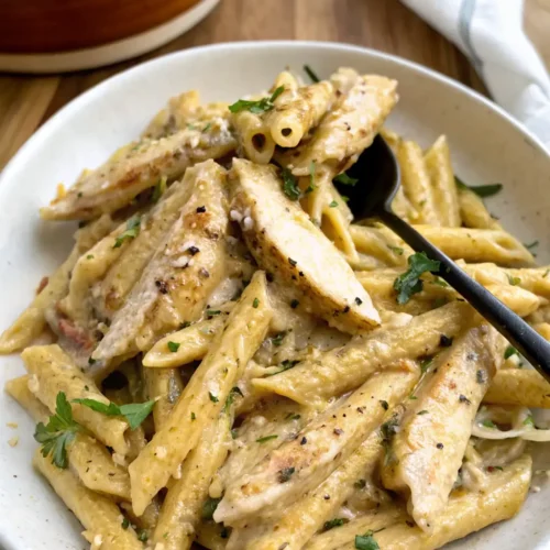 serving bowl filled with Garlic Parmesan Chicken Pasta and sliced seasoned chicken, garnished with fresh parsley and ready to be enjoyed with a black spoon.
