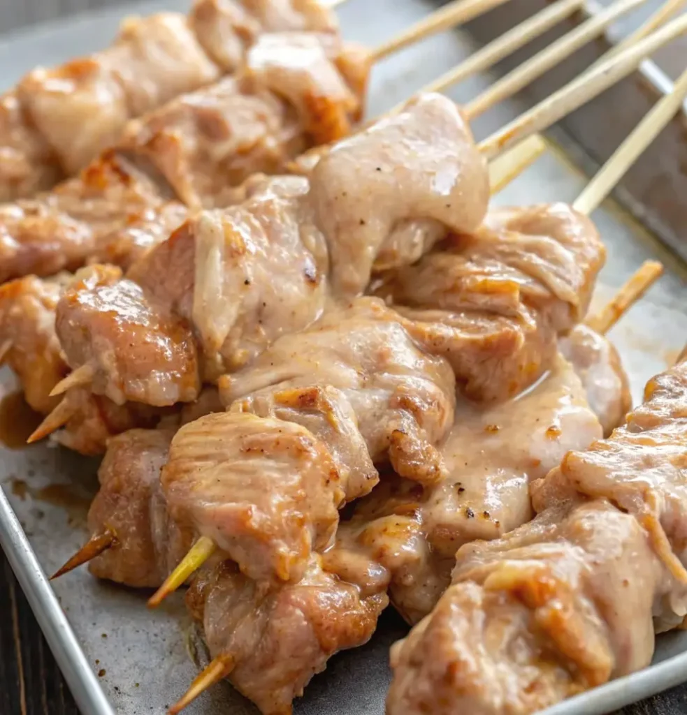 chicken skewers coated, Bang Bang marinade, ready for cooking, arranged closely together on a rectangular metal baking tray.