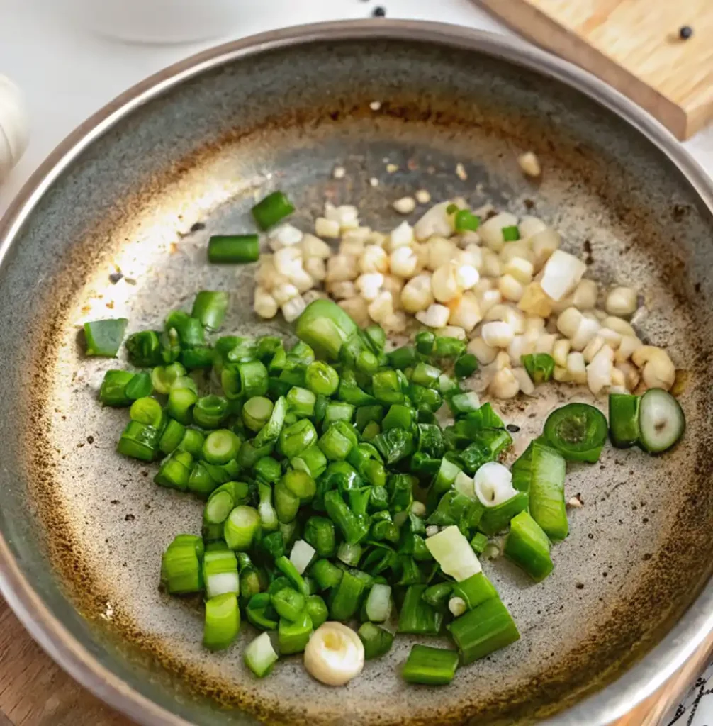 Close-up of a well-used metal pan containing piles of fresh, chopped green onions and minced garlic,