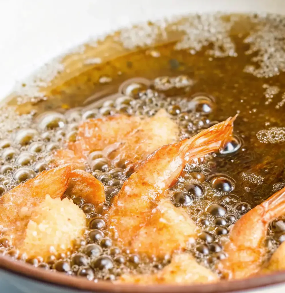 flour-coated shrimp turning golden and crisp as they deep-fry in bubbling oil, a key step in preparing homemade Salt and Pepper Shrimp.