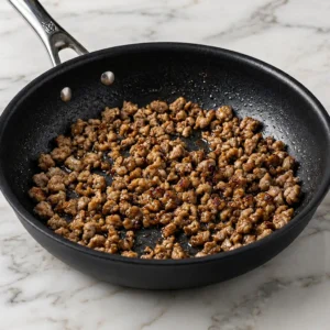 Seasoned ground sausage browned in a black nonstick skillet over a white marble countertop