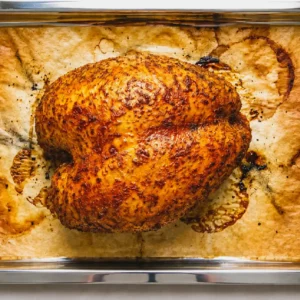 Fully cooked smoked turkey breast with golden brown skin resting on butcher paper inside a metal sheet pan after smoking.