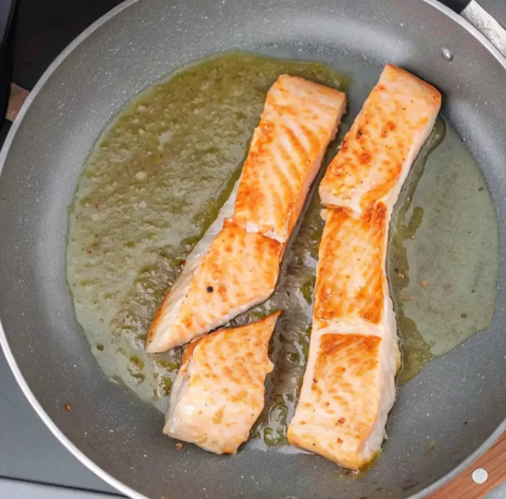 salmon fillet are searing in a non-stick pan. The fish has developed a golden-brown crust