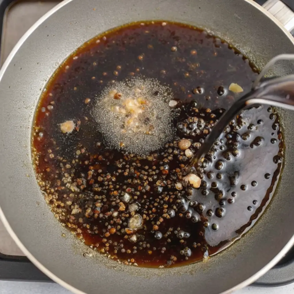 The rich salmon sauce is prepared in a silver pan. The sauce is boiled and contains soy sauce, small pieces of garlic and minced ginger, and some spices.