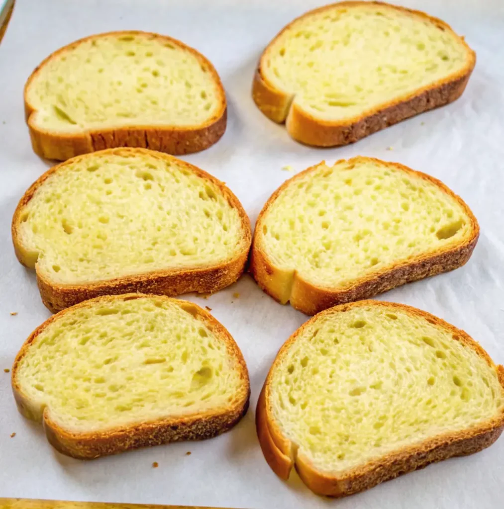 Six thick slices of Texas Toast are laid out on a baking sheet lined with parchment paper.