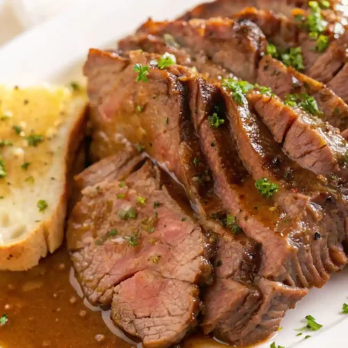 Slices of juicy Pikes Peak roast beef topped with rich brown gravy, served on a white plate