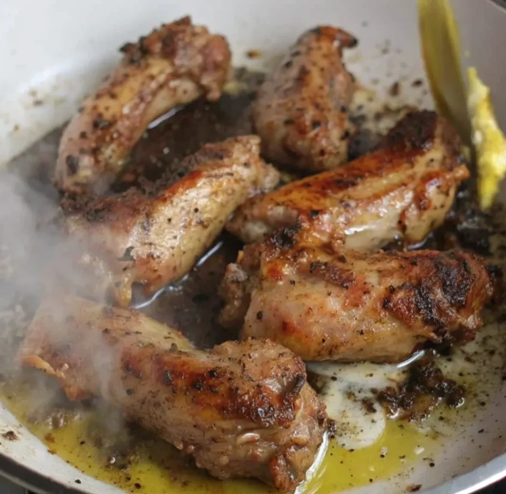 Seared and seasoned turkey necks are browning in a white pan, sizzling in rendered fat or oil,