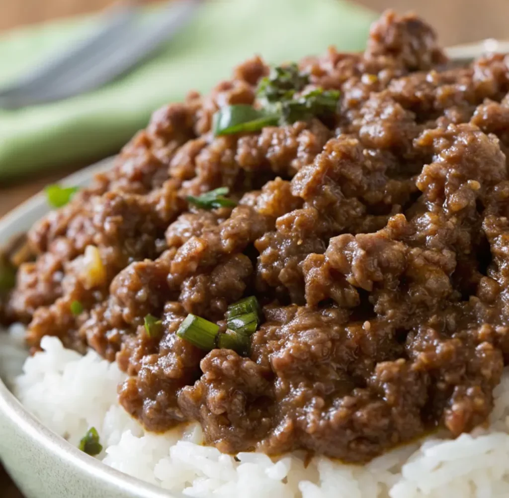 A serving bowl containing delicious dark brown minced meat, a recipe for Wagyu minced beef, garnished with chopped green onions, served on top of a pile of white rice.