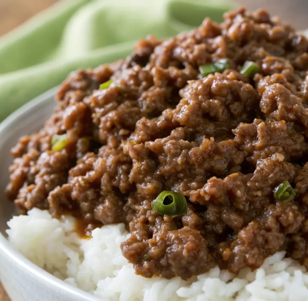 A serving bowl containing delicious dark brown minced meat, a recipe for Wagyu minced beef, garnished with chopped green onions, served on top of a pile of white rice.