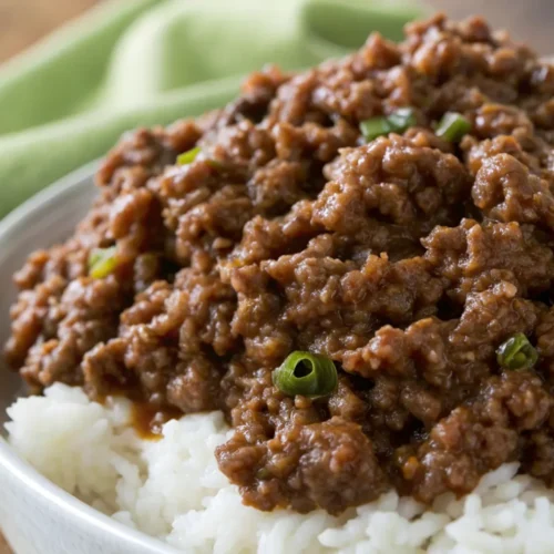 A serving bowl containing delicious dark brown minced meat, a recipe for Wagyu minced beef, garnished with chopped green onions, served on top of a pile of white rice.