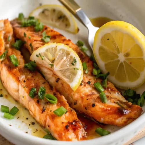 Delicious crispy golden salmon belly recipe garnished with fresh herbs and lemon served in a white dish for a special dinner