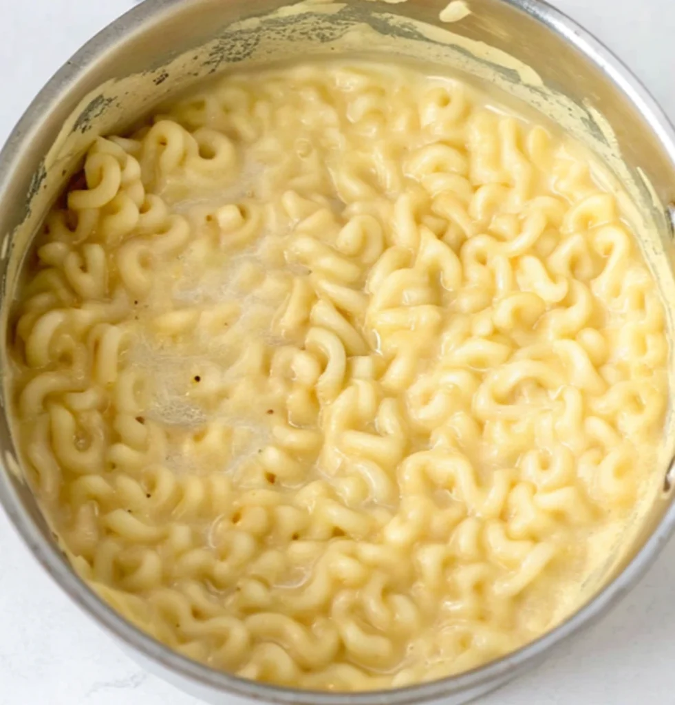 Cooked macaroni submerged and covered with cream cheese sauce inside a metal pot. This forms the basic mixture for the Brisket Mac and Cheese.