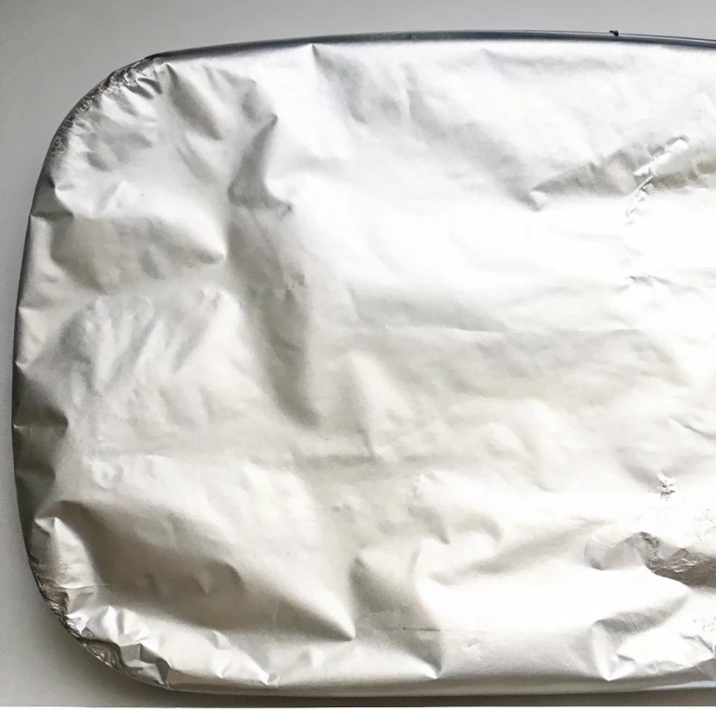 A rectangular baking dish No Peek Beef Tips is completely covered by a sheet of crinkled aluminum foil,