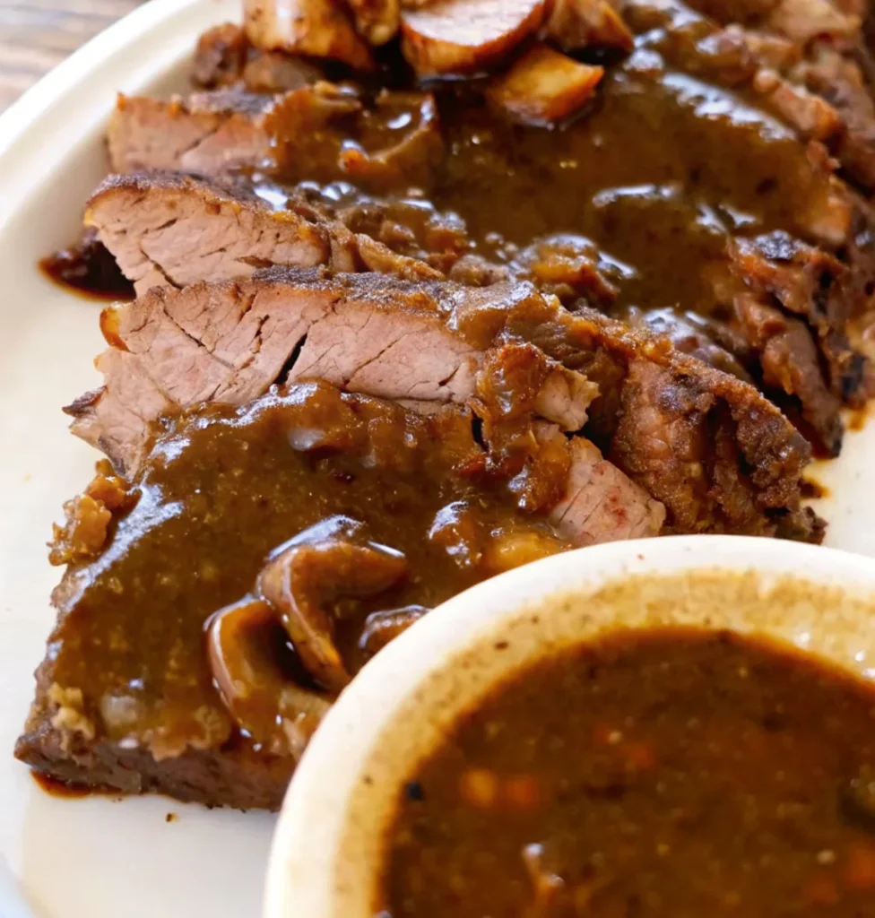 Thinly sliced Pikes Peak Roast Beef recipe, perfectly cooked and smothered in a thick, mushroom-rich gravy, ready to be served.