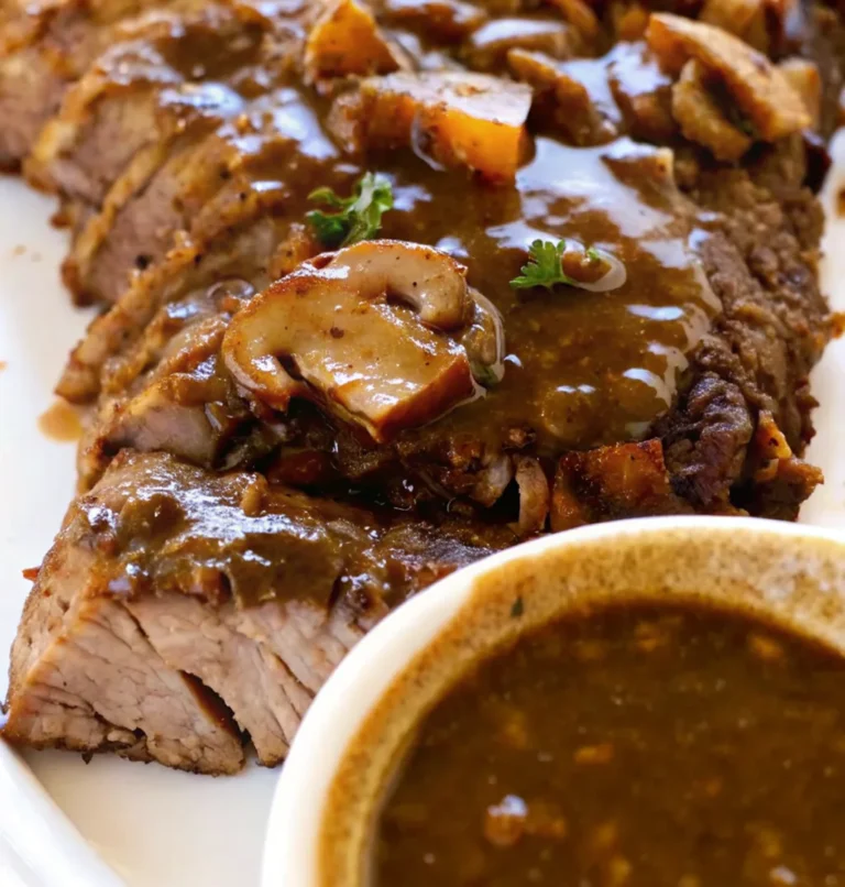 Thinly sliced Pikes Peak Roast Beef recipe, perfectly cooked and smothered in a thick, mushroom-rich gravy, ready to be served.