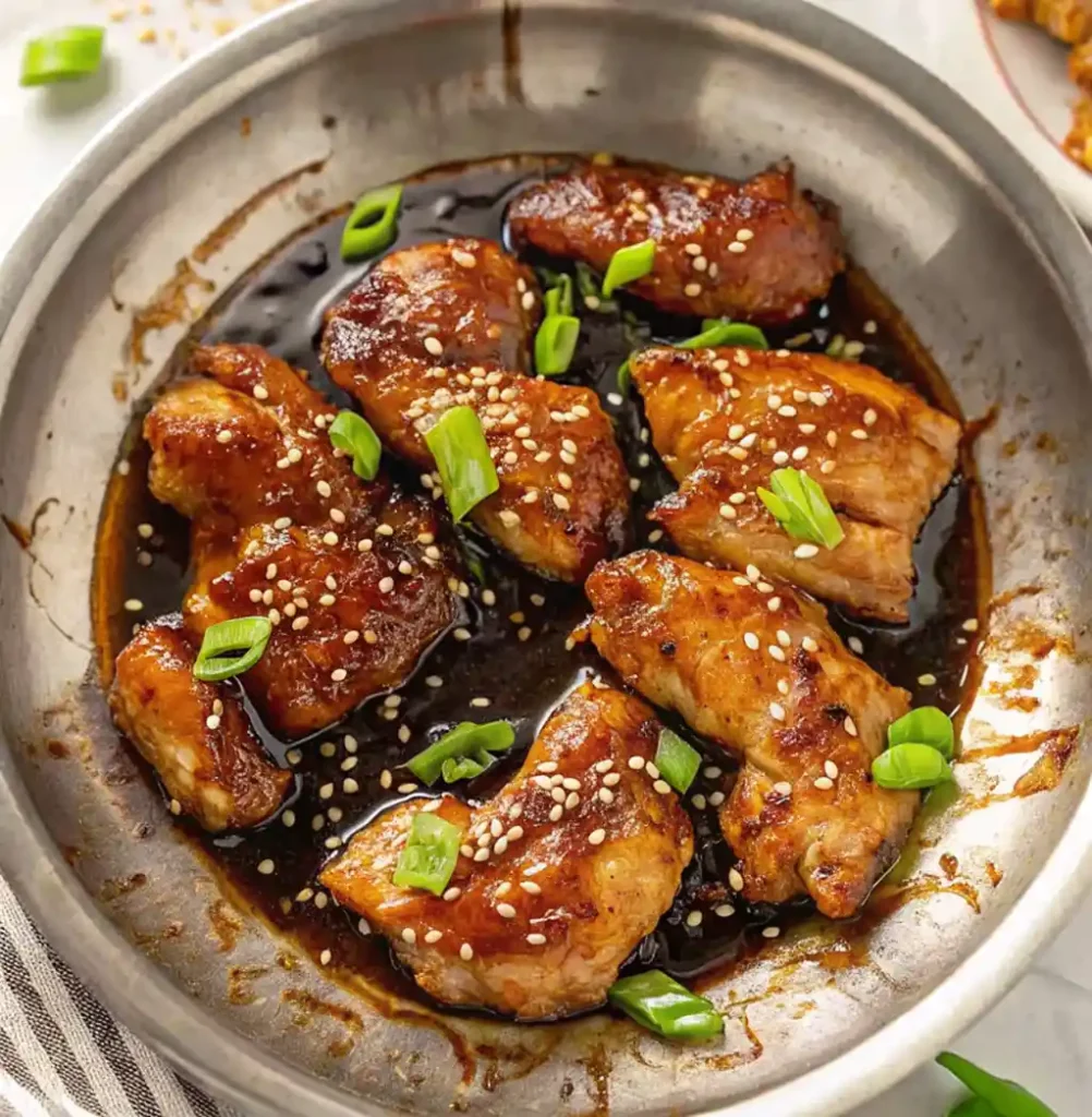 Grilled teriyaki chicken pieces, coated with teriyaki sauce, sesame seeds and sliced spring onions, in a metal pan. It gives Panda Express's grilled teriyaki chicken the perfect flavour.