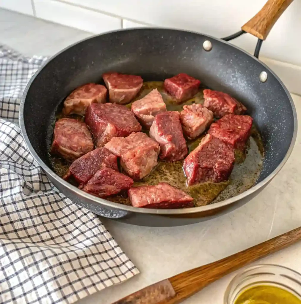 Cubed steak browning in a skillet with olive oil, developing a flavorful crust for crockpot steak.