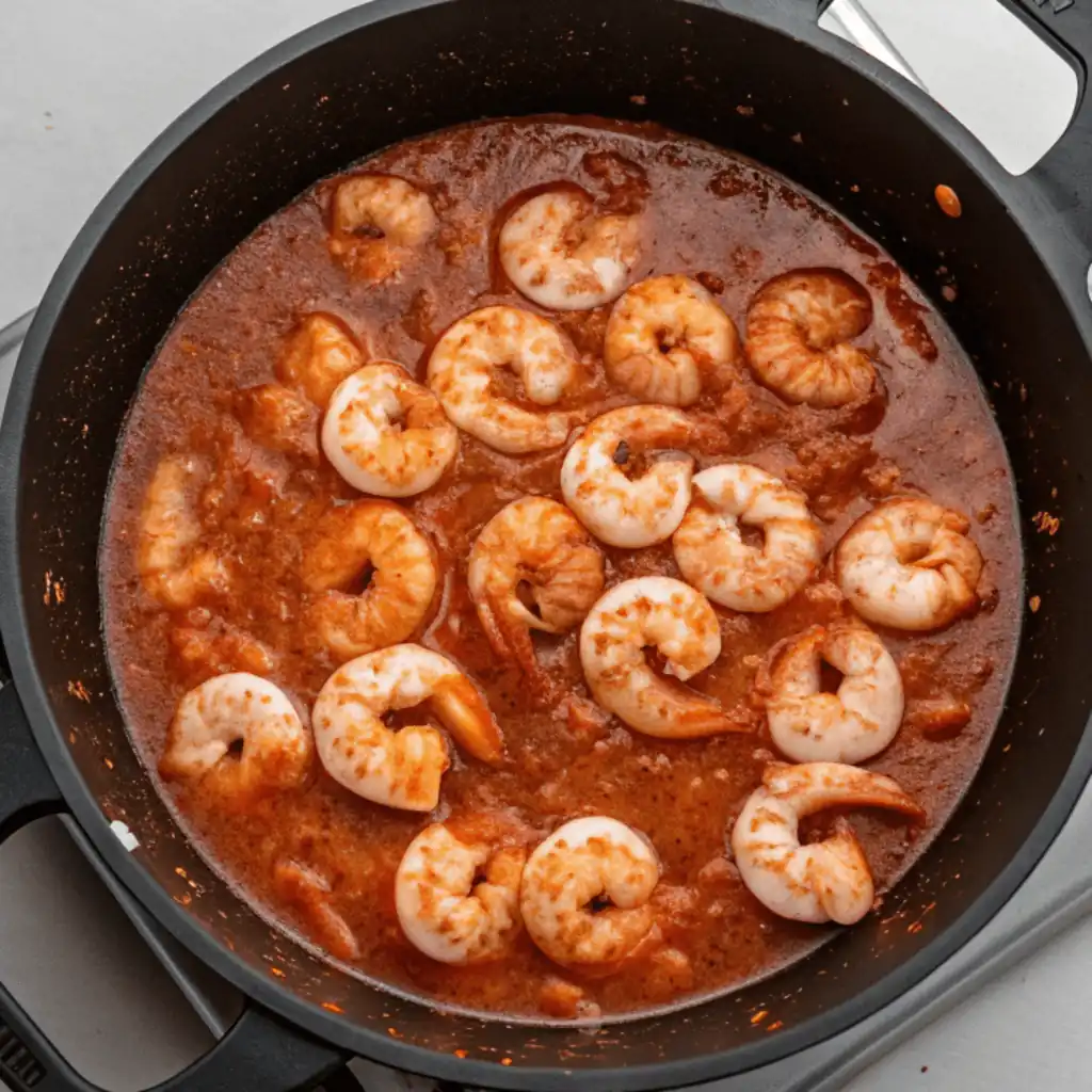Cooked, pink shrimp simmering in a rich Vindaloo Sauce within a black pot.