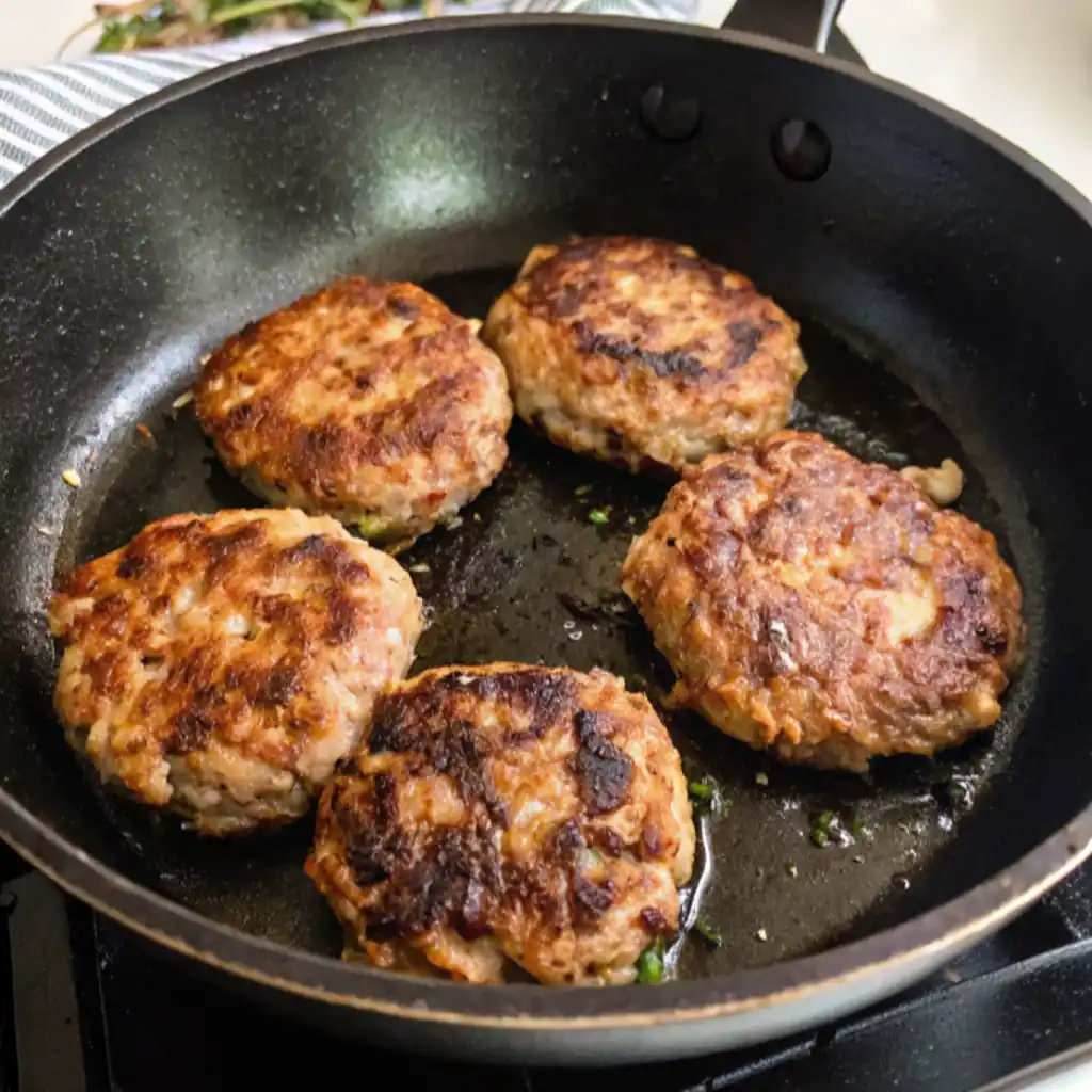 Turkey sausage patties cooked in a black skillet on the stovetop, golden and crispy