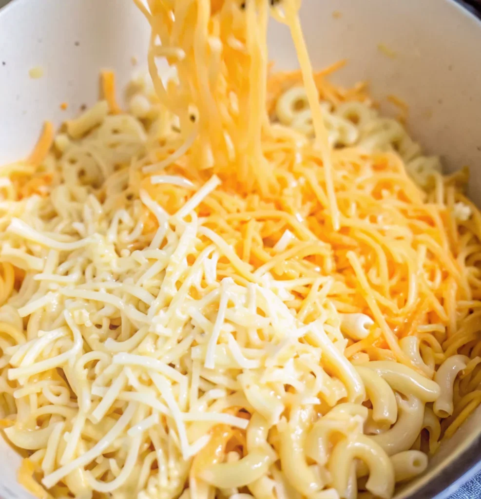cooked cavatappi pasta in a bowl being mixed with copious amounts of shredded cheddar and white cheeses for a mac and cheese component.