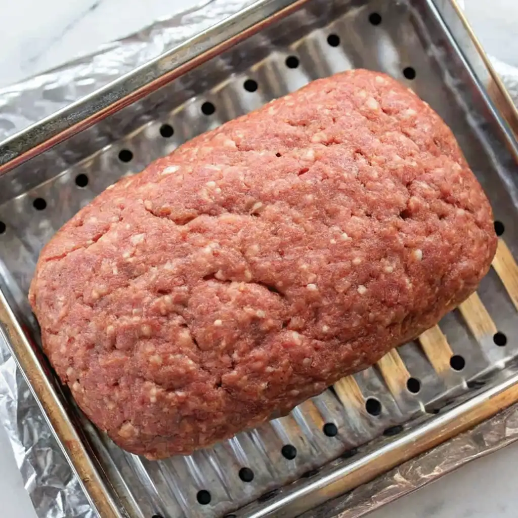 Meatloaf Without Breadcrumbs resting inside a perforated metal insert designed to drain grease during cooking. It's sitting over a foil-lined pan.