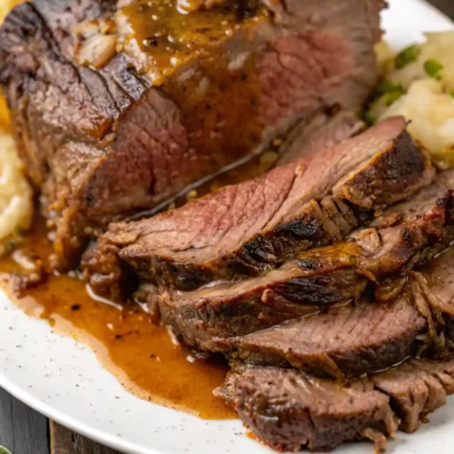Tender slices of Pikes Peak Roast served with gravy and mashed potatoes on a white plate