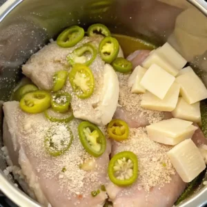 Raw chicken in an Instant Pot topped with pepperoncini peppers and cubes of butter, ready for cooking.