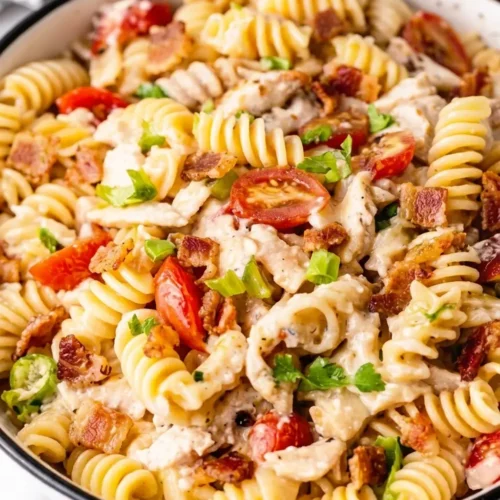 A vibrant, fully assembled Chicken Bacon Ranch Pasta Salad tossed in a creamy dressing with rotini noodles, juicy cherry tomato halves, shredded chicken, bacon pieces, and fresh parsley.