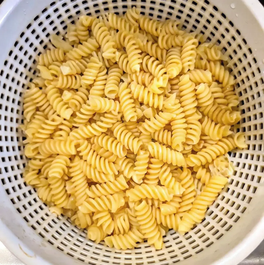  Cooked yellow “Rotelli” pasta is being drained in a white plastic colander. The spiral-shaped pasta fills the bowl.