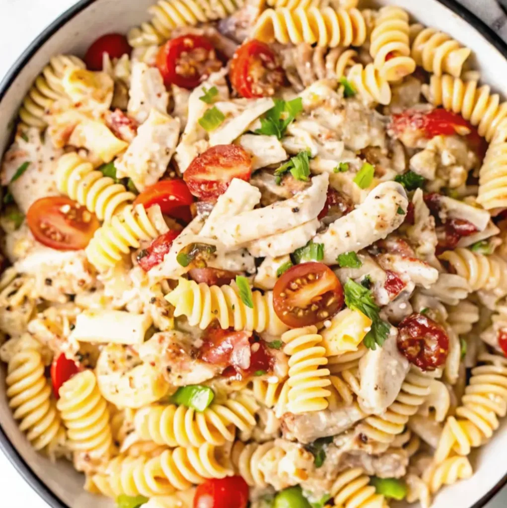 A vibrant, fully assembled Chicken Bacon Ranch Pasta Salad tossed in a creamy dressing with rotini noodles, juicy cherry tomato halves, shredded chicken, bacon pieces, and fresh parsley.