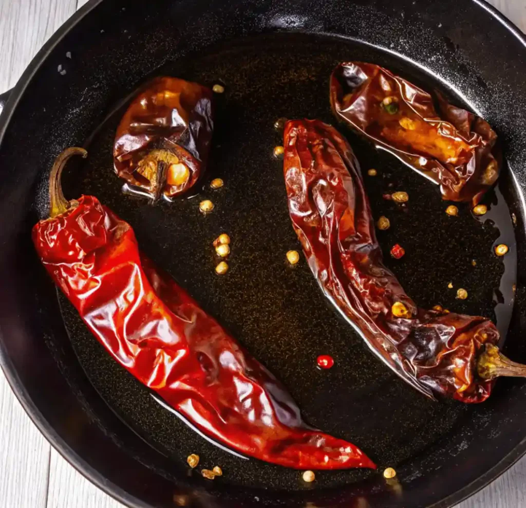 dried red chili peppers, two brighter red and two darker, being toasted in hot oil in a skillet, key for making Chicken birria tacos.