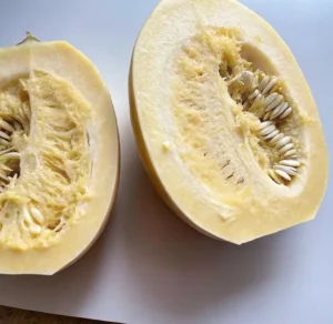 Two halves of a raw Mashed Potato Squash (Sweet Dumpling Squash) are cut open, revealing the stringy, pale-yellow flesh and the cluster of seeds in the center cavity.