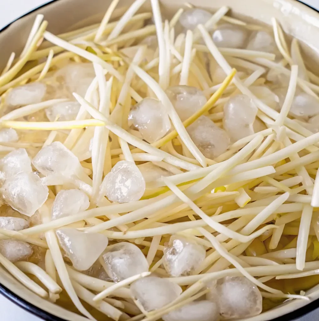 shoestring potato strips soaking in a bowl of water with ice cubes. The soaking process helps to remove excess starch for crispier fries.